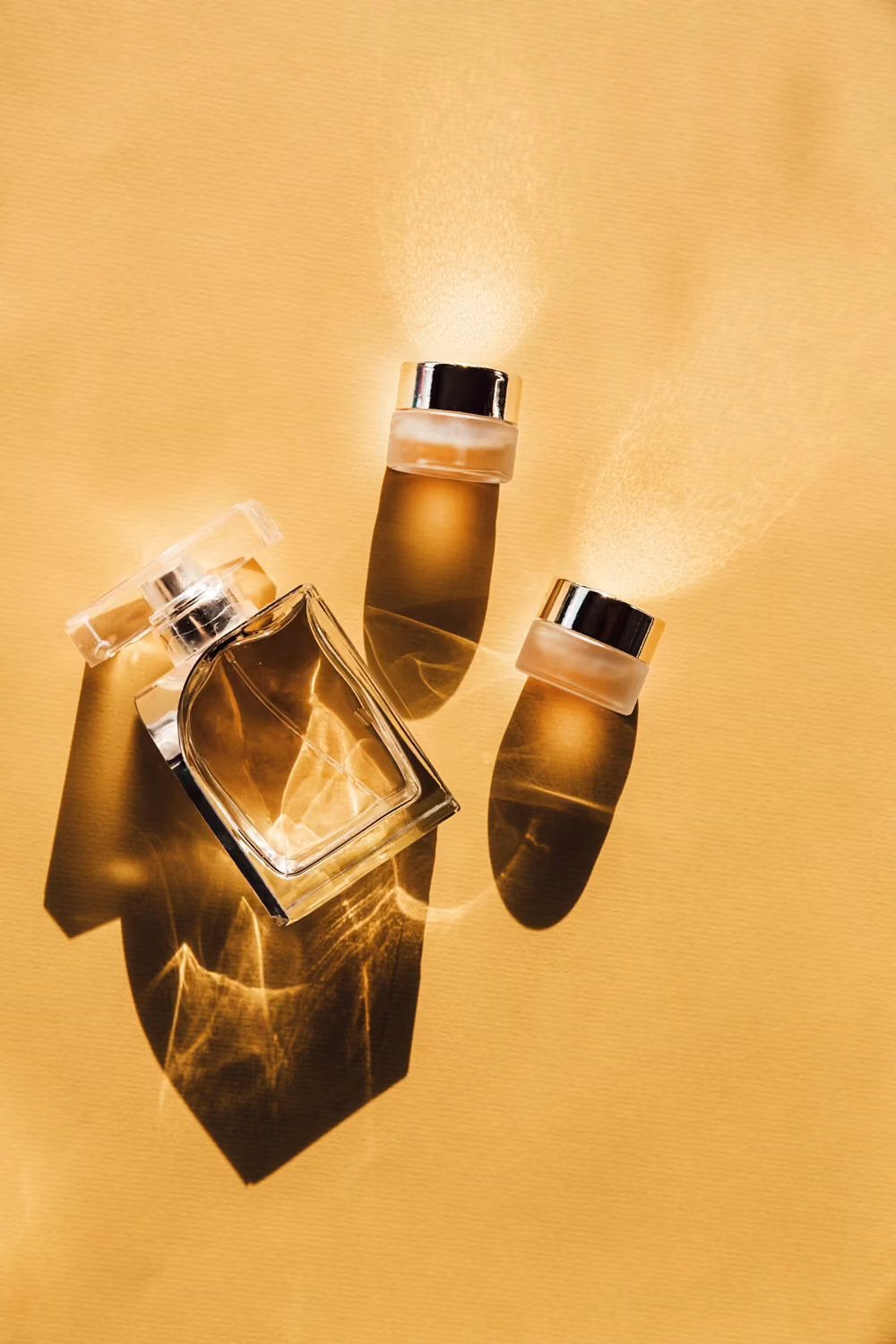 A glass perfume bottle and two small cosmetic jars on a yellow surface