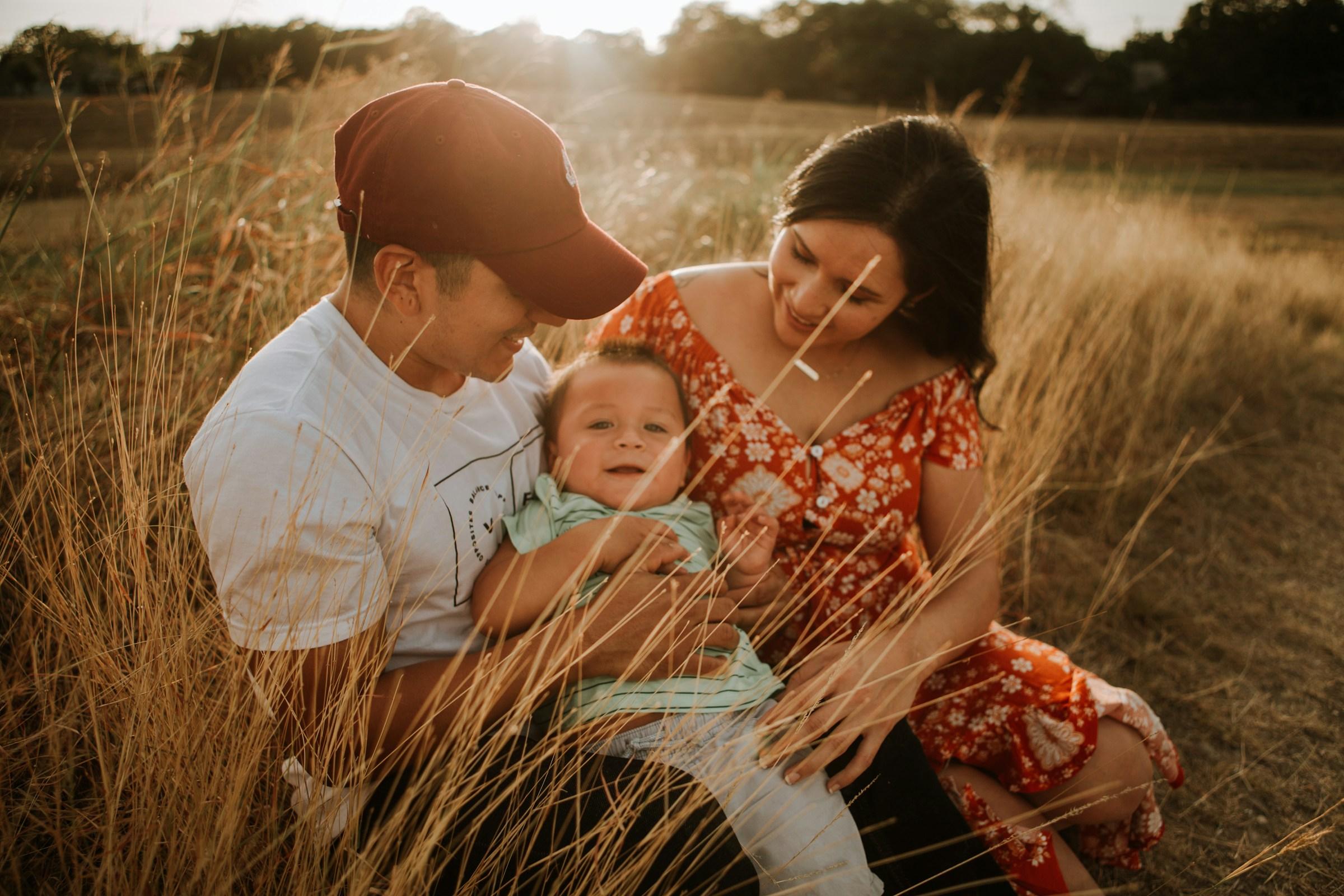 Young family smiling together in tall grass at golden hour