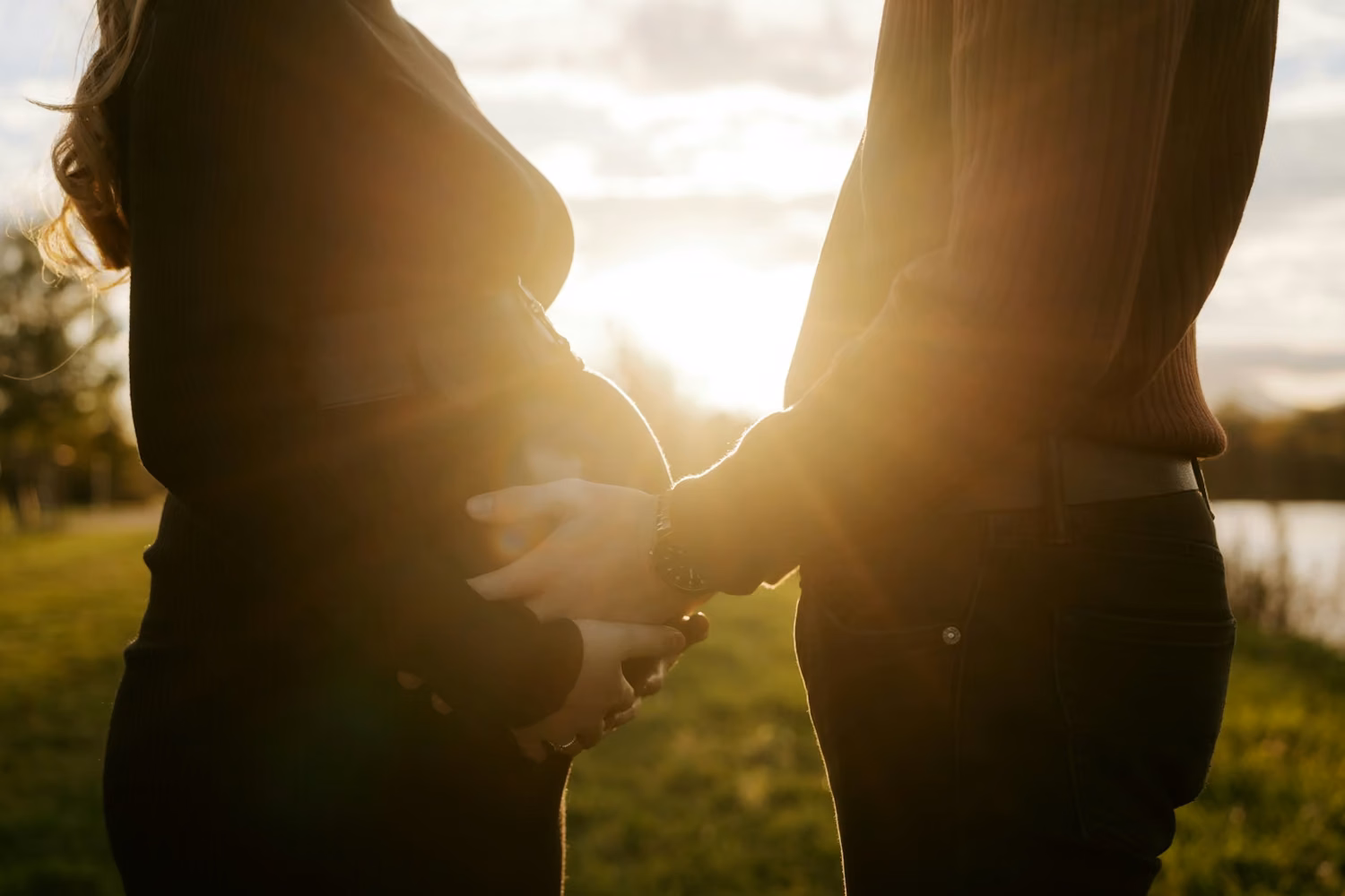 Couple holding pregnant belly at sunset